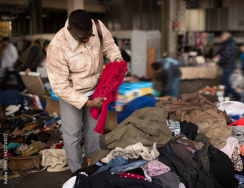 african american guy chooses sacond hands clothes at flea market