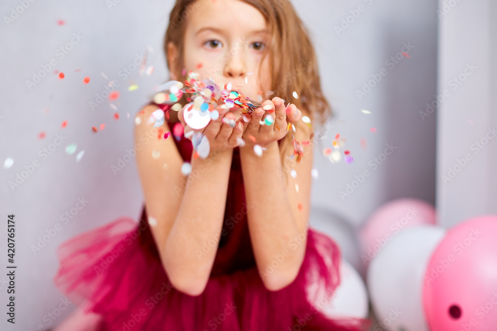 Beautiful little girl blows up multicolored confetti, having fun at home birthday party Beautiful little girl blows up multicolored confetti, having fun at home birthday party