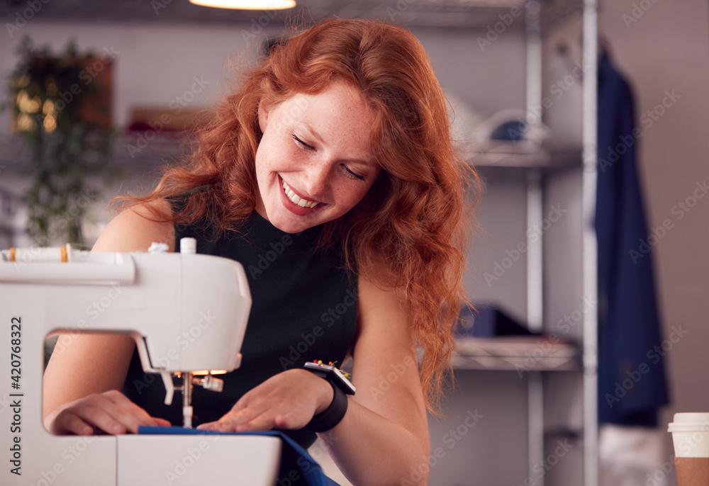 Smiling Female Student Or Business Owner Working In Fashion Using Sewing Machine In Studio