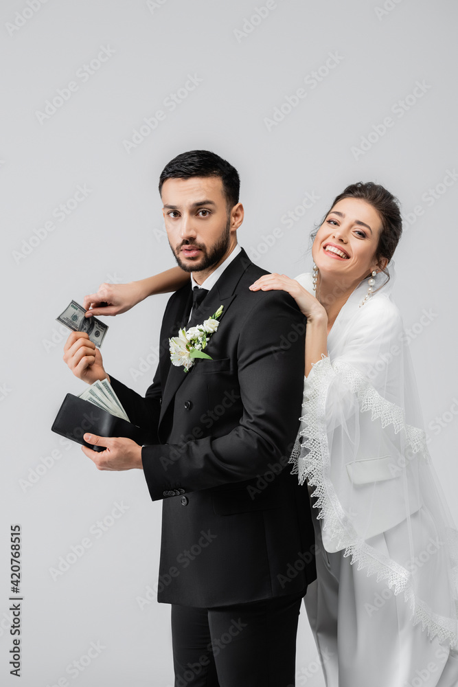 Smiling bride taking money from arabian boyfriend with wallet isolated on grey Smiling bride taking money from arabian boyfriend with wallet isolated on grey