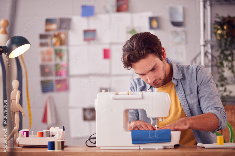 Male Student Or Business Owner Working In Fashion Using Sewing Machine In Studio Male Student Or Business Owner Working In Fashion Using Sewing Machine In Studio