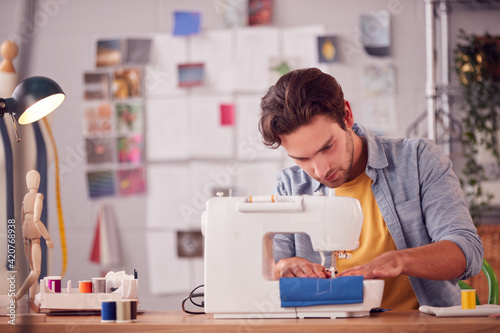 Male Student Or Business Owner Working In Fashion Using Sewing Machine In Studio