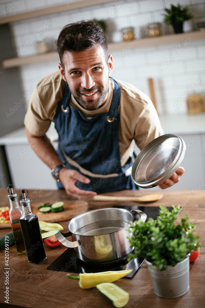 Happy smiling man preparing tasty meal. Young man cooking in the kitchen..