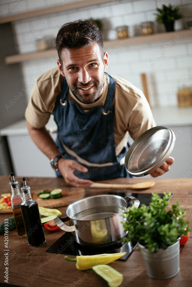 Happy smiling man preparing tasty meal. Young man cooking in the kitchen..