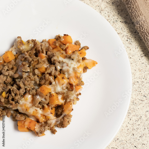 A white plate with a healthy, nutritious dinner with ground turkey, sweet potatoes, and mozzarella cheese ready to eat with a silver fork and brown tan napkin.