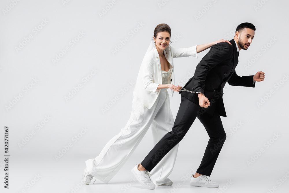 Smiling bride stopping running muslim groom in handcuffs on white background Smiling bride stopping running muslim groom in handcuffs on white background