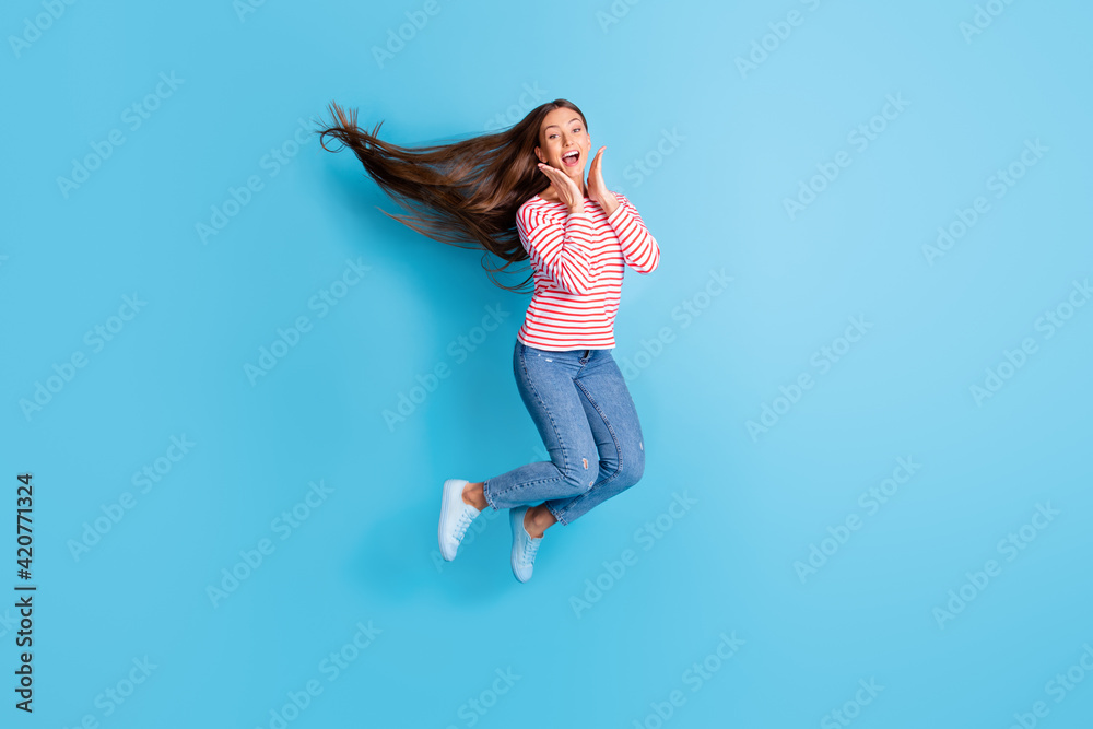 Full length body size photo jumping girl amazed overjoyed touching cheeks smiling isolated vibrant blue color background