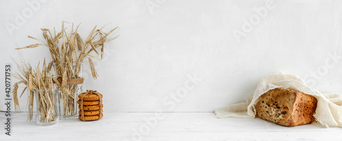 White kitchen banner - oatmeal cookies, grain bread and ears of grain on a white table.