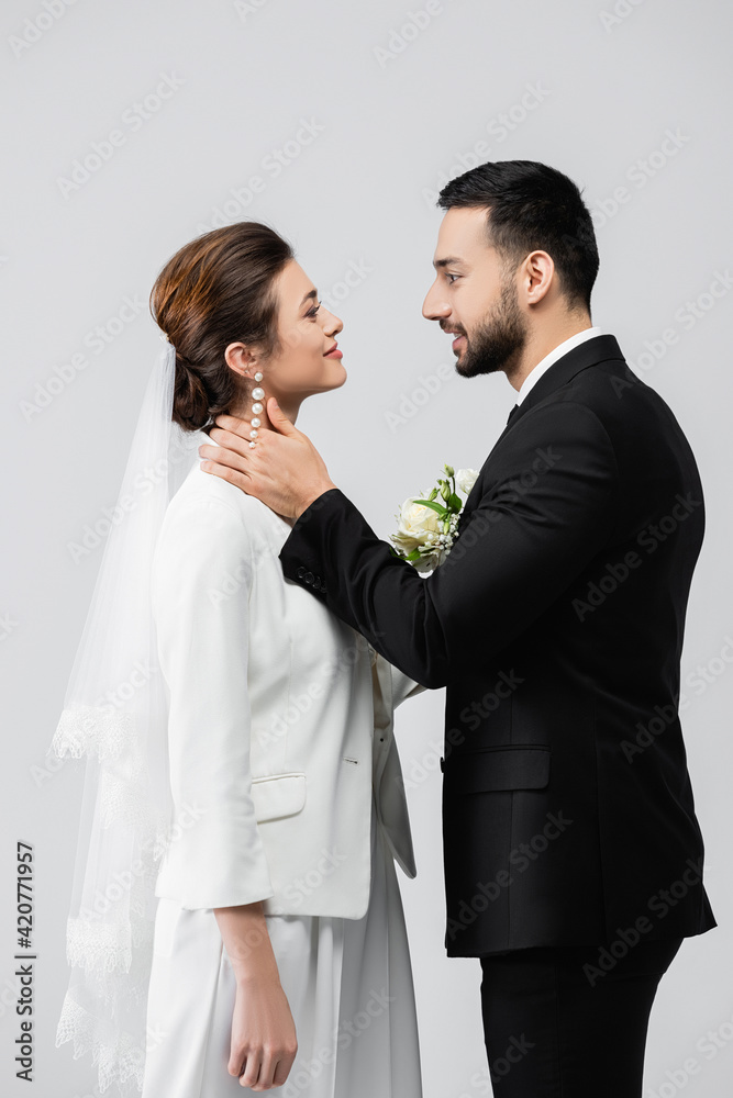Side view of muslim groom touching neck of smiling bride isolated on grey Side view of muslim groom touching neck of smiling bride isolated on grey
