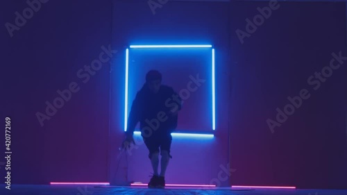 Person in windbreaker and red cap dancing to breakdance. blue rectangle neon background . Flickering neon background . man dancing to breakdance in night club