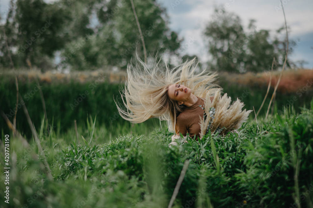 Blonde woman poses with fluttering in wind hair on meadow. Blonde woman poses with fluttering in wind hair on meadow.