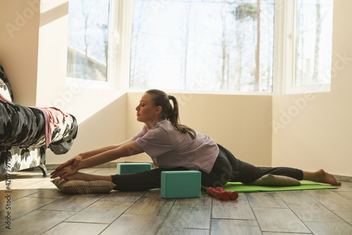 A young woman sits on a twine. The girl performs stretching exercises at home on the fitness mat. Home sport online