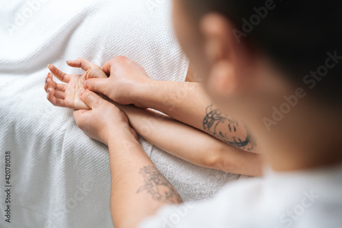 Back view of male physiotherapist doing finger and palm massage to young woman at spa salon. Man physiotherapist doing relaxing massage female on hand, palm and fingers.