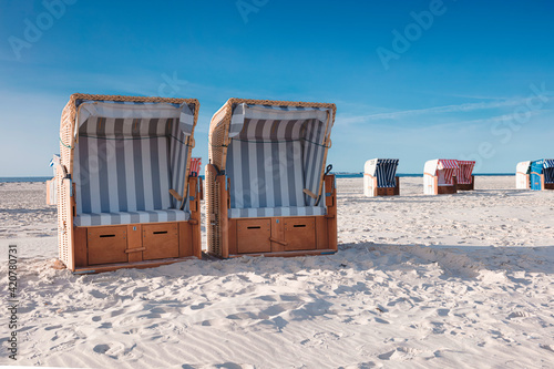 Couple of striped roofed wicker beach chairs standing in white sand on beach in hot summer sunshine.