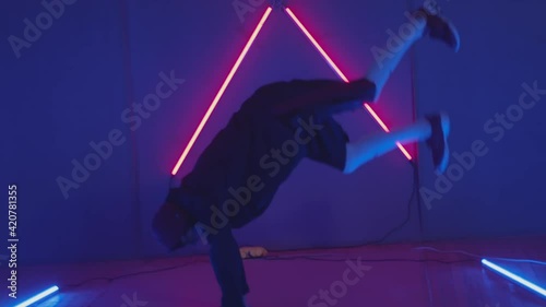 Person in windbreaker and red cap dancing to breakdance. red triangle neon background . Flickering neon background . man dancing to breakdance in night club
