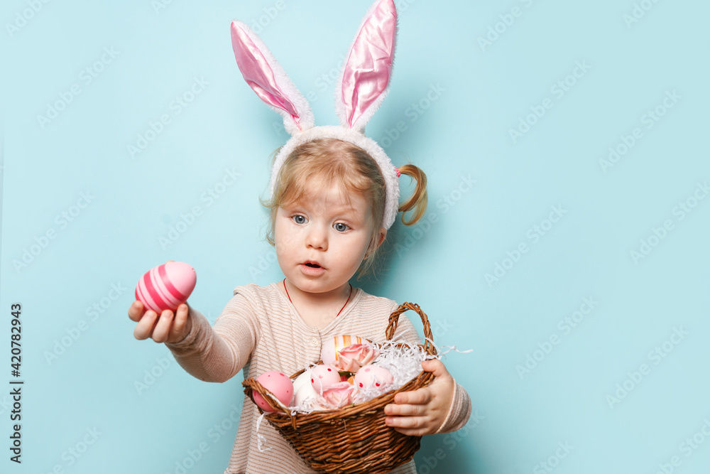 Portrait of a cute little girl dressed in Easter bunny ears holding colorful eggs on blue background