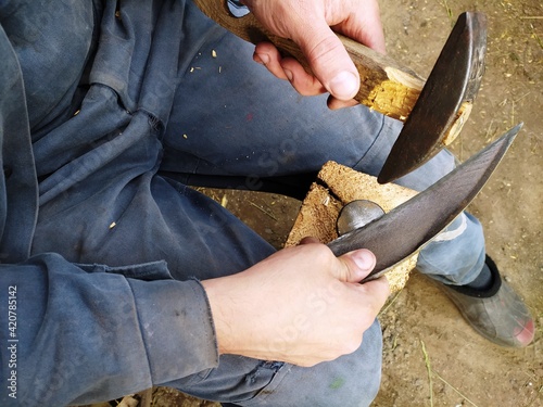 Hands of craftsman with knife sharpening a blade scythe