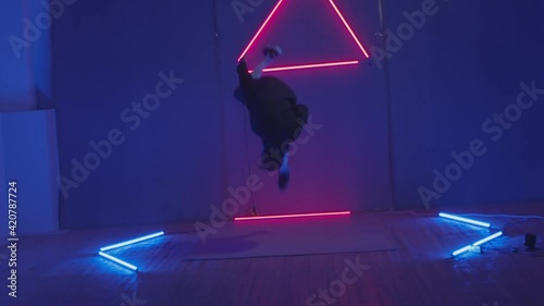 Person in windbreaker and red cap dancing to breakdance. red triangle neon background . Flickering neon background . man dancing to breakdance in night club