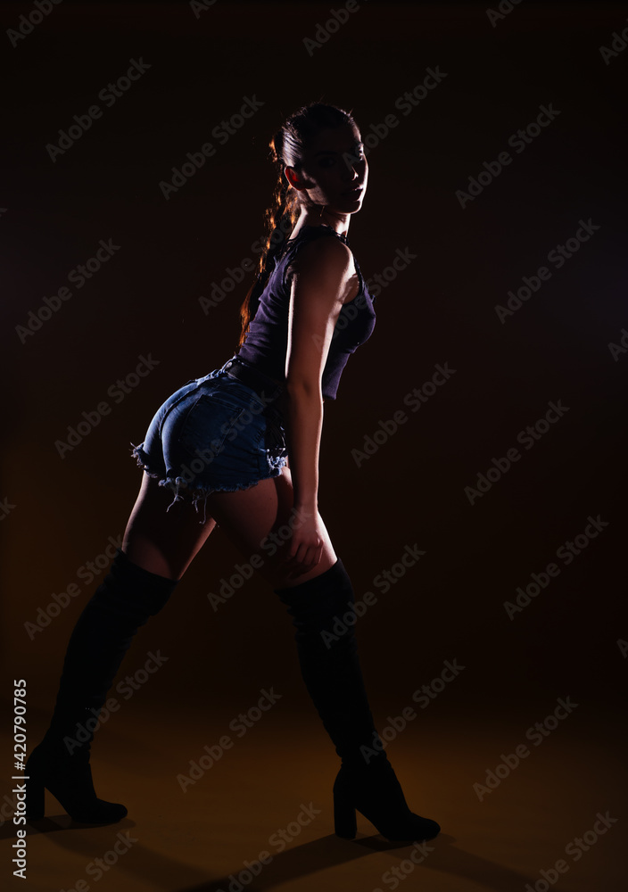 High-contrast silhouette picture of a sexy female model posing on a dark background