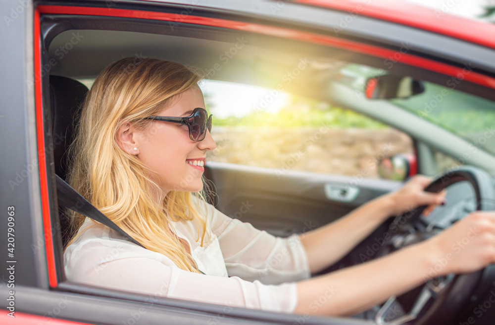 Happy beautiful woman is driving a red car.