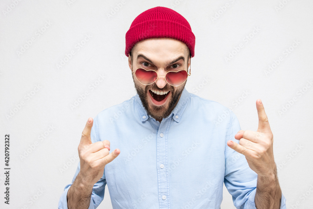 Naklejka premium Winning man, bearded man in love wears glasses shows the goat gesture, portrait, white background