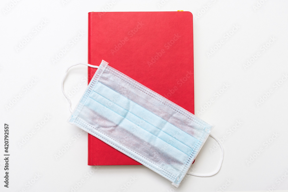 Red textbook and medical mask, white background, copy space, top view Red textbook and medical mask, white background, copy space, top view