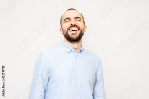 Laughing young bearded man with closed eyes from laughter, concept of positive emotions of people, white background © Анастасия Семашко