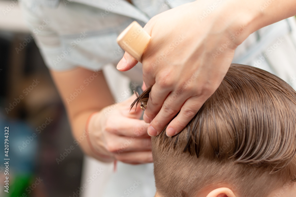 caring female hands of a mother with a comb and scissors make a fashionable haircut for her son at home during the second lockdown. selective focus