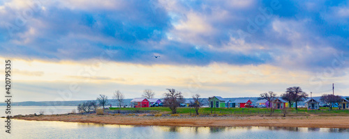 Multicolored cabins on the lakeshore at sunrise with bold skies