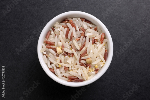 mixed low glycaemic index healthy rice grain basmati millet buckwheat red rice in small white ceramic bowl over black background photo