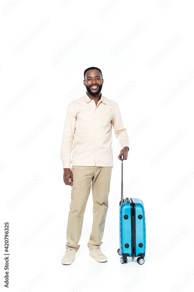 happy african american man looking at camera while standing with travel bag on white happy african american man looking at camera while standing with travel bag on white