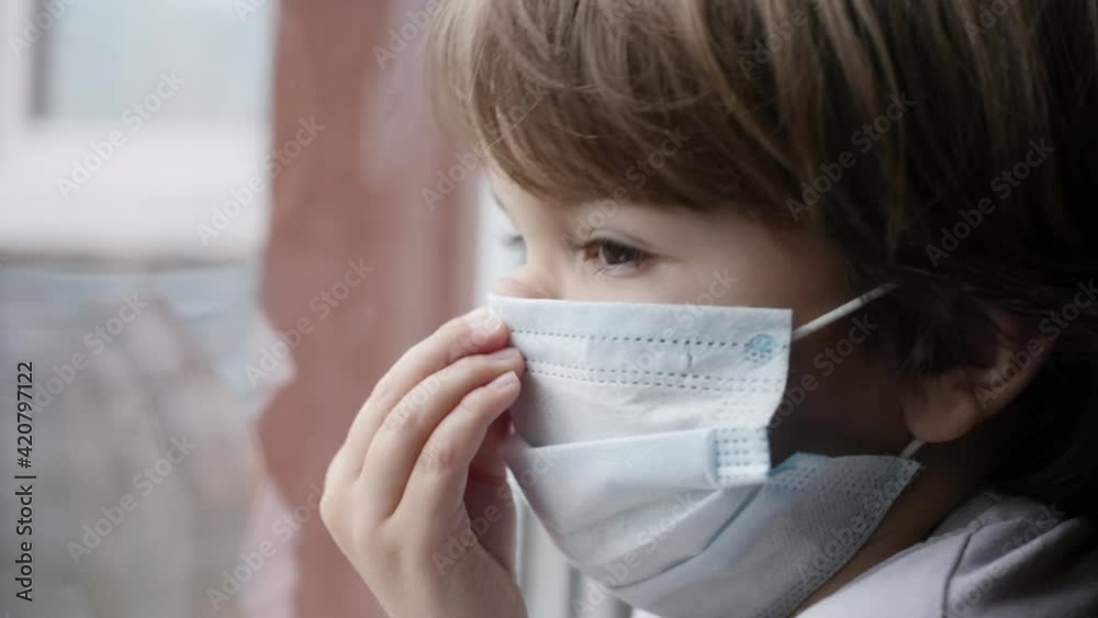 Little Child Boy With Protective Mask, Sad Looking Through Window Worried About Covid-19 Lockdown. Kid In Protection Mask Looking Out Window Home. Quarantine Coronavirus Social Distancing Little Child Boy With Protective Mask, Sad Looking Through Window Worried About Covid-19 Lockdown. Kid In Protection Mask Looking Out Window Home. Quarantine Coronavirus Social Distancing