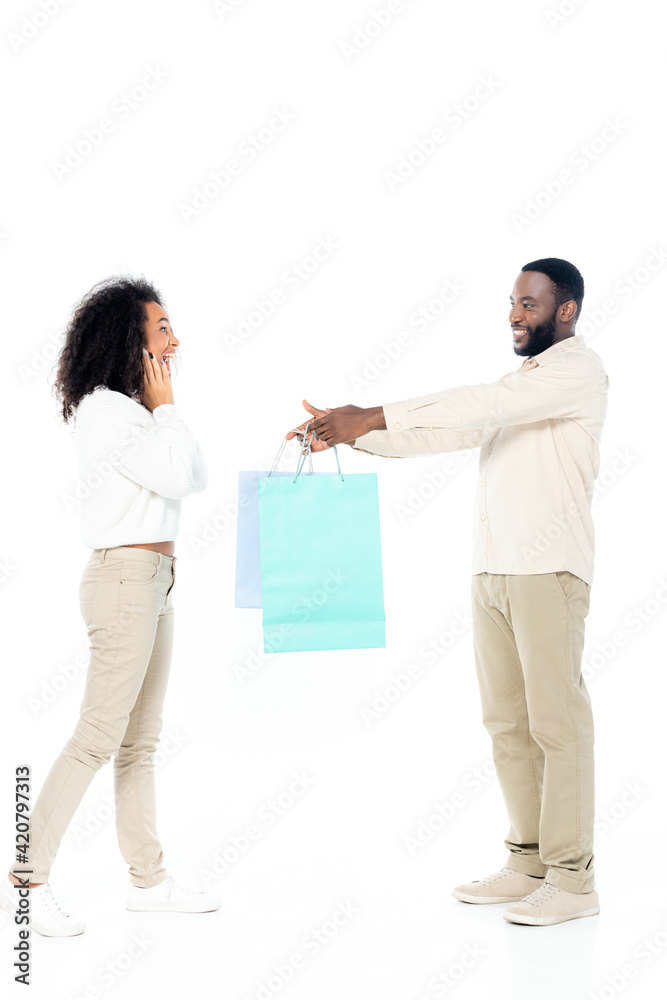 smiling african american man giving shopping bags to amazed wife on white smiling african american man giving shopping bags to amazed wife on white