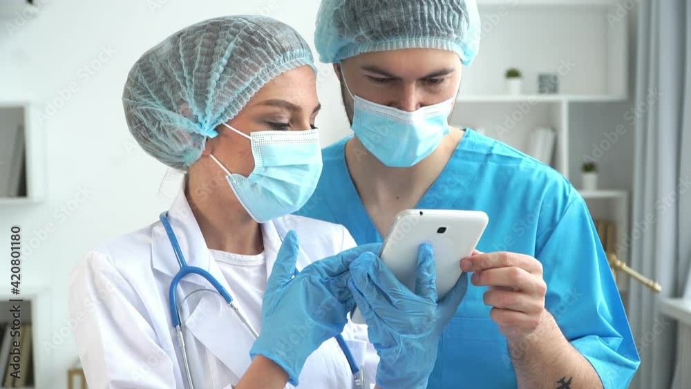 Medical team of doctors in white coats and protective masks work on digital tablet in clinic. Coronavirus, covid-19 Medical team of doctors in white coats and protective masks work on digital tablet in clinic. Coronavirus, covid-19