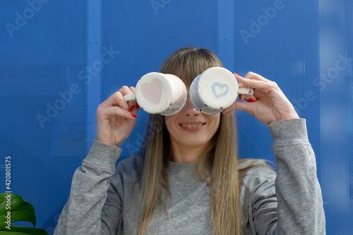 Obraz na plátne Two ceramic teacups with hearts painted on the bottom in the hands of a smiling woman