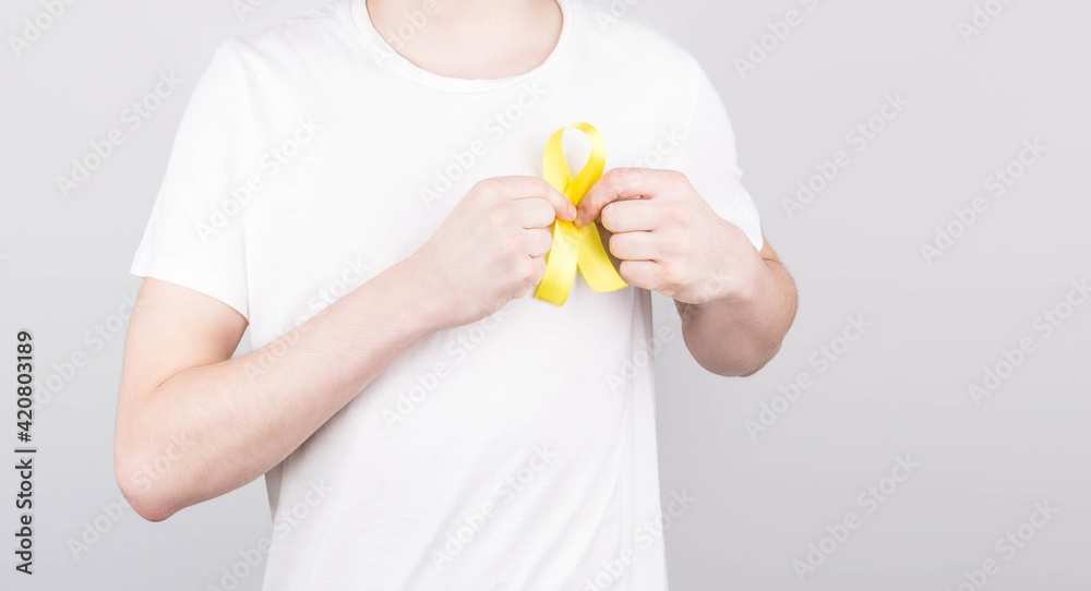 Young man in white t-shirt holding yellow ribbon awareness symbol for suicide, sarcoma bone cancer, bladder cancer, liver cancer and childhood cancer concept. Health care. Young man in white t-shirt holding yellow ribbon awareness symbol for suicide, sarcoma bone cancer, bladder cancer, liver cancer and childhood cancer concept. Health care.