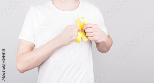 Young man in white t-shirt holding yellow ribbon awareness symbol for suicide, sarcoma bone cancer, bladder cancer, liver cancer and childhood cancer concept. Health care.