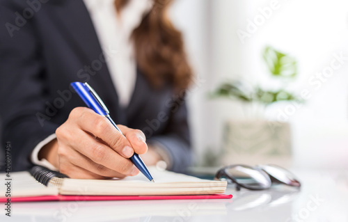 Business woman writing something on notebook. Close-up