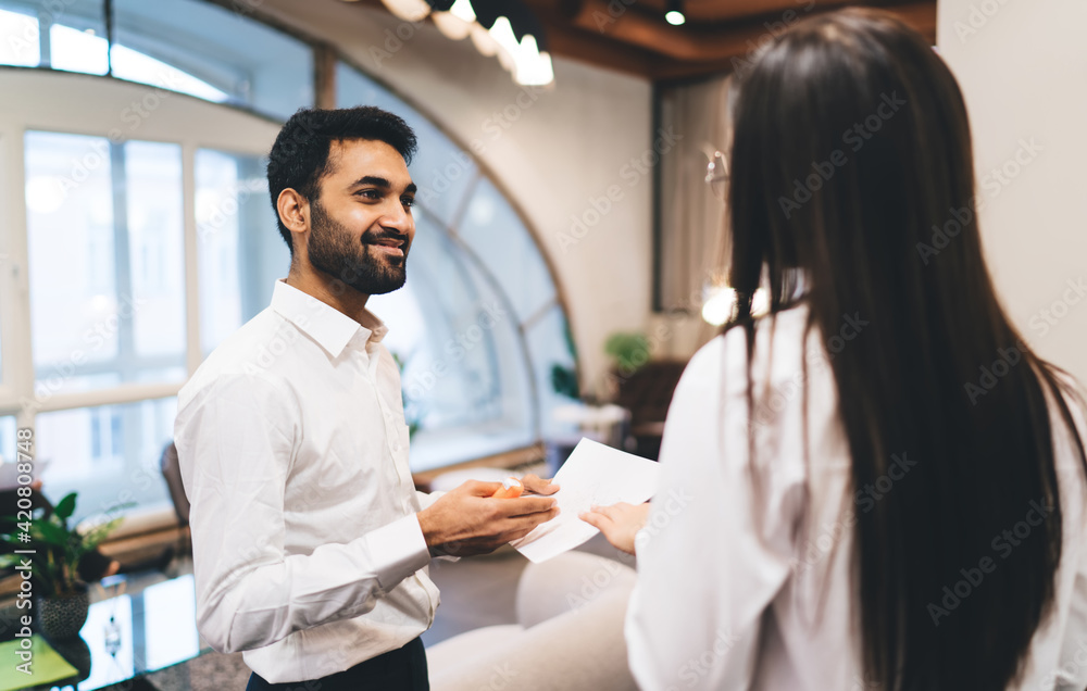 Fototapeta premium Smiling ethnic employee talking to unrecognizable colleague in office