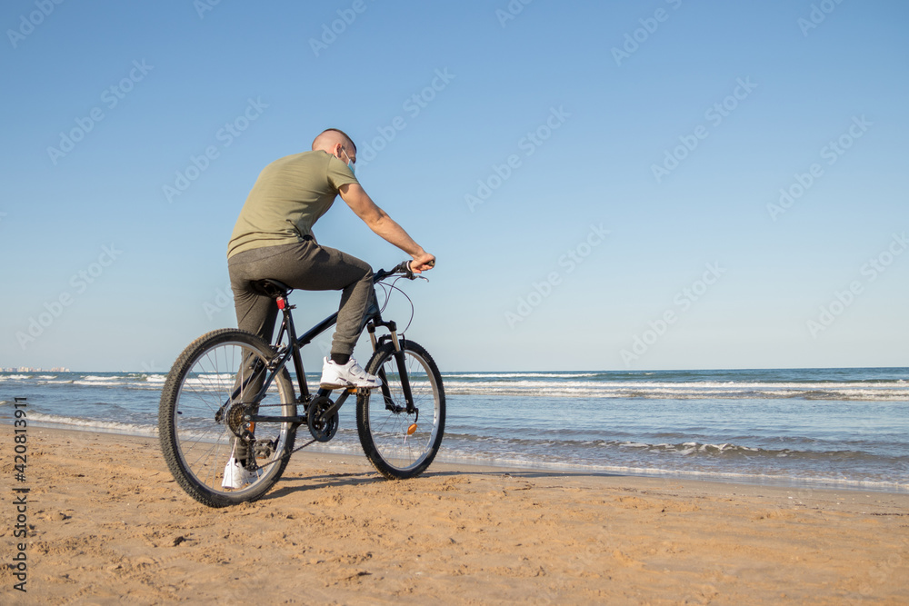Boy with green shirt and mask arriving at his destination after a bike ride to rest on the beach Boy with green shirt and mask arriving at his destination after a bike ride to rest on the beach