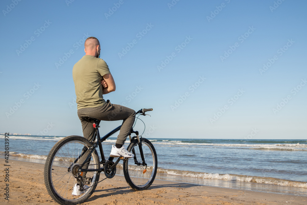 Boy with green shirt and mask arriving at his destination after a bike ride to rest on the beach Boy with green shirt and mask arriving at his destination after a bike ride to rest on the beach