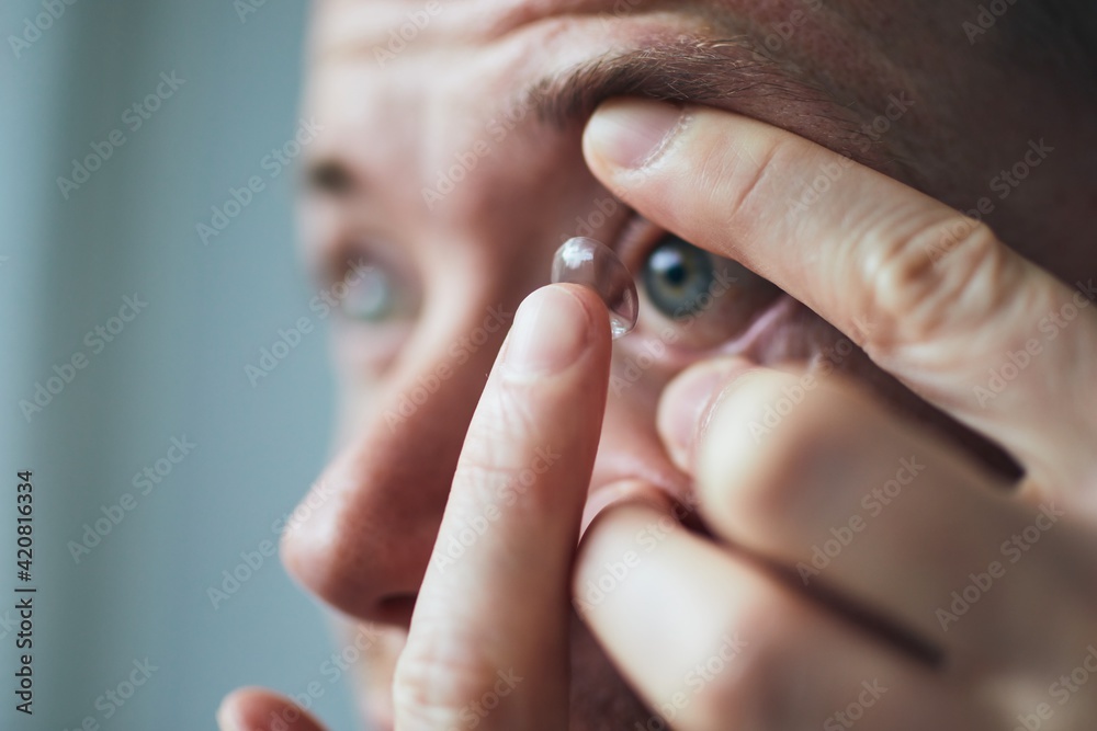 Young man putting contact lens on eye. Themes eyesight and daily routine. - obrazy, fototapety, plakaty 