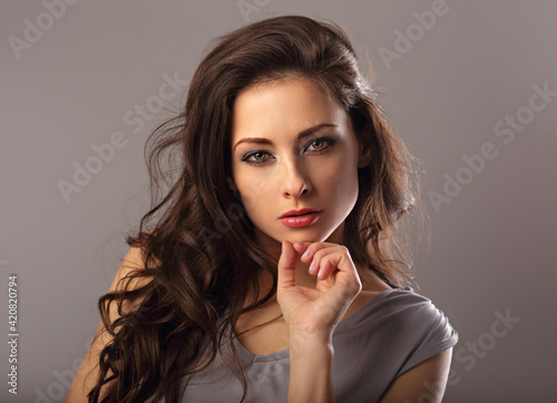 Beautiful mysterious woman makeup face and healthy volume brown hair with wisdom emotional look on brown color background with empty copy space. Closeup