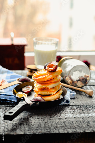pancakes with a sweet plum and honey in a frying pan on a blue wooden background. a glass of milk. rustic style. copy space for text