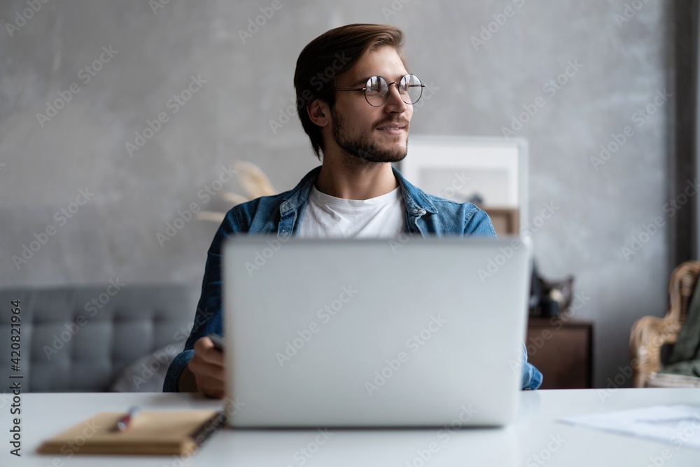 Thoughtful man looking away while sitting at his working place in office Thoughtful man looking away while sitting at his working place in office