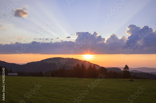 Amazing sunset sky above the Jura Mountains, Switzerland. Beautiful cloudscape with visible sun rays and light over the hills and field, interesting cloud shape. 