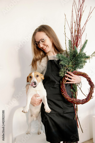 Cute young woman in glasses kisses and hugs her jack russell terrier dog. Love between owner and dog. Making New Year's decor and wreath. Decorator work and lifestyle