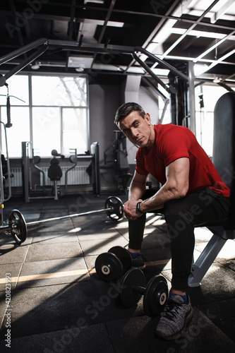 Vertical shot of a mature male athlete resting after working out with heavy dumbbells, copy space