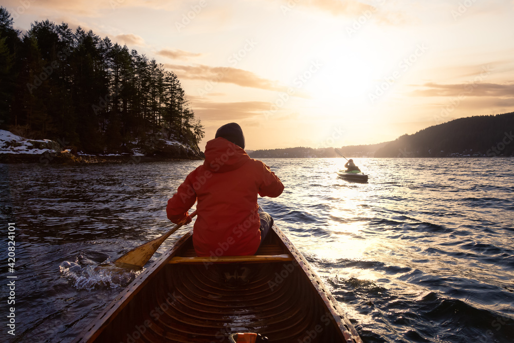 Adventure Man on a wooden canoe is paddling in the ocean. Dramatic Sunset Sky Art Render. Taken in Indian Arm, North of Vancouver, British Columbia, Canada.