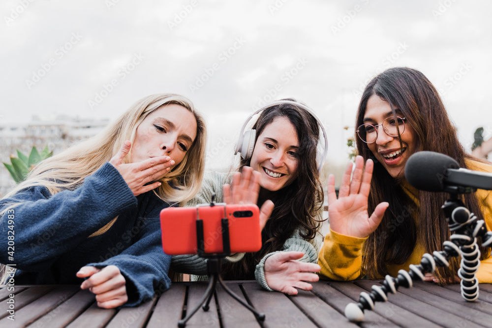 Multiracial people streaming online podcast with mobile phone outdoors in summer day - Main focus on right girl face Multiracial people streaming online podcast with mobile phone outdoors in summer day - Main focus on right girl face